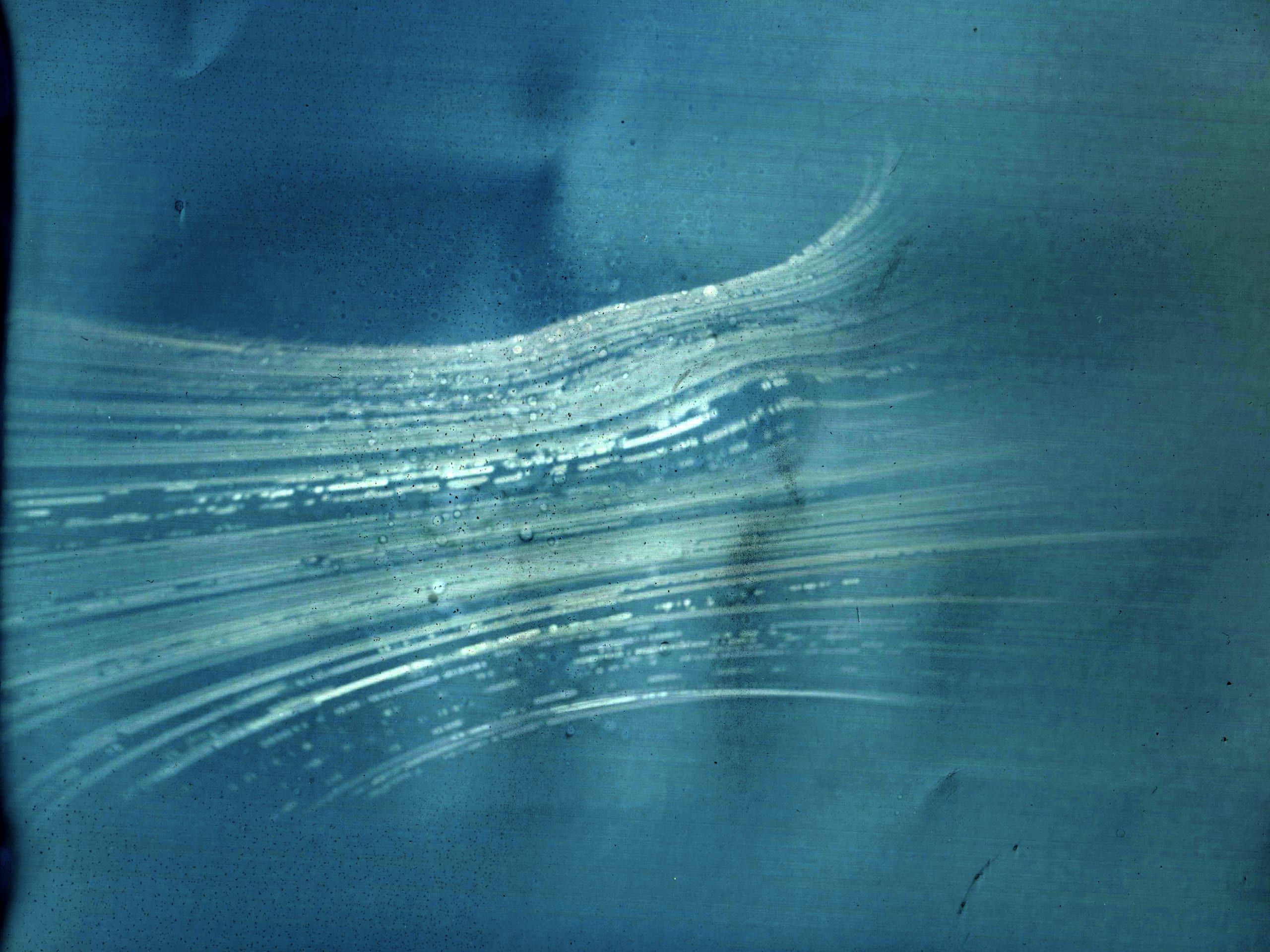 Blue-toned solargraph with white streaks tracing daily sun paths arcing across the sky over months