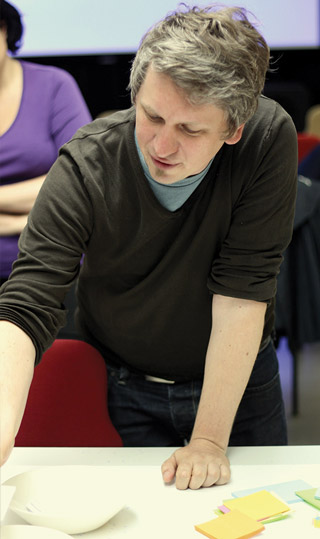 Moritz Stefaner at work, leaning over a table arranging colored sticky notes in a workshop